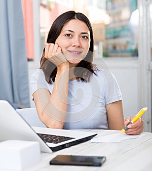 Young girl student with laptop and papers working at home