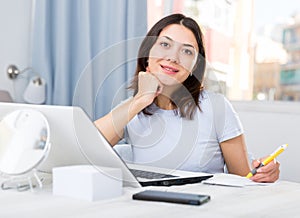 Young girl student with laptop and papers working at home