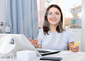 Young girl student with laptop and papers working at home