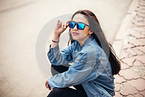 Young girl student is sitting on the pavement. Wear jeans and drink coffee