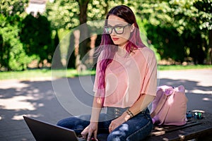 Young girl is studying in the spring park, sitting on the wooden bench and browsing on her laptop