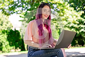 Young girl is studying in the spring park, sitting on the wooden bench and browsing on her laptop