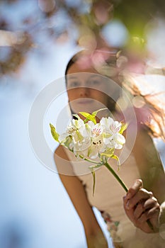 Young girl in summer dress extending her arm towards viewer holding a white flower. Face covered partially