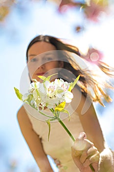 Young girl in summer dress extending her arm towards viewer holding a white flower while her long hair is affected by the wind
