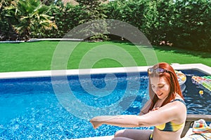 young girl sunbathing by the pool, sitting on an amaca applying sun cream on her arms. woman enjoying summer holidays