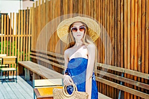 Young girl in sunglasses in a straw hat on a background of a wooden wall. Summer mood, relaxation