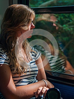 Young girl in sunset lighting traveling in train car and her reflection in window