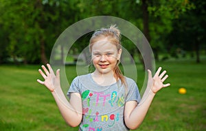 A young girl is surprised in the park in summer against the background of trees and green grass