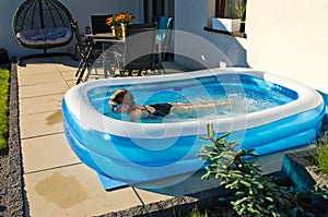 Young girl swimming in inflatable swimming pool on home backyard terrace. Staycation sta home concept photo
