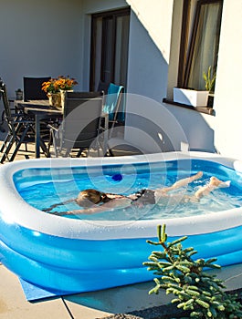 Young girl swimming in inflatable swimming pool on home backyard terrace. Staycation sta home concept