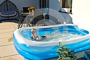 Young girl swimming in inflatable swimming pool on home backyard terrace. Staycation sta home concept