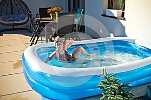 Young girl swimming in inflatable swimming pool on home backyard terrace. Staycation sta home concept photo