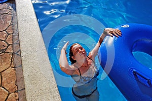 The young girl swims in the pool with a rubber ring. She has thrown back the head and rinses hair. photo