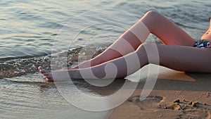 Young girl in a swimsuit sitting on the wet sand on the sea coast