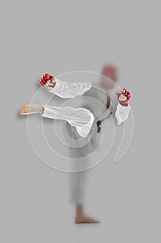 Young girl, taekwondo practitioner strikes forcibly with the foot isolated over grey background. Concept of sport