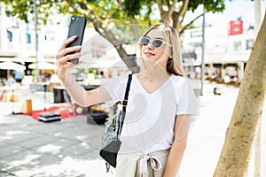 Young girl take selfie from hands with phone on summer city street. Urban life concept.