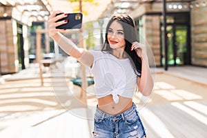 Young girl take selfie from hands with phone on summer city street. Urban life concept
