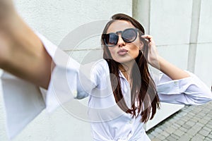 Young girl take selfie from hands with phone on summer city street. Urban life concept