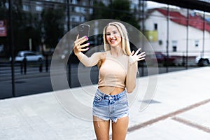 Young girl take selfie from hands with phone on summer city street. Urban life concept