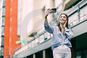 Young girl take selfie with phone on summer city street. Urban life concept