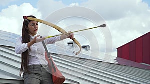 Young girl takes aim with a bow on the roof of a house