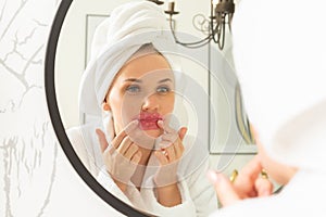 A young girl takes care of her face in the bathroom, a woman stands in front of the mirror puts lip patches on her face