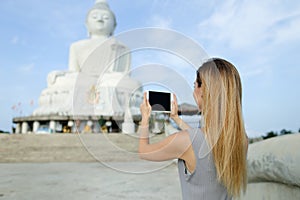 Young girl taking photo by tablet of white statue of Buddha in Phuket.