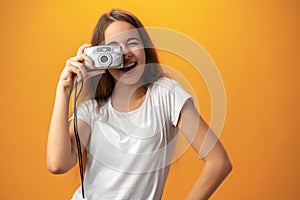 Young girl taking pictures on camera against yellow background.