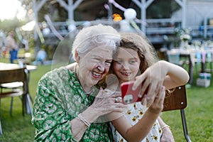 Young girl taking selfie with elderly grandmother at garden party. Love and closeness between grandparent and grandchild