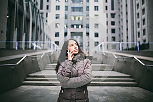 Young girl talking on mobile phone in courtyard business center. girl with long dark hair dressed in winter jacket in cold weather