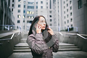 Young girl talking on mobile phone in courtyard business center. girl with long dark hair dressed in winter jacket in cold weather