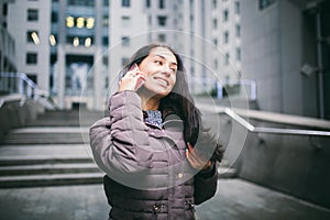 Young girl talking on mobile phone in courtyard business center. girl with long dark hair dressed in winter jacket in cold weather