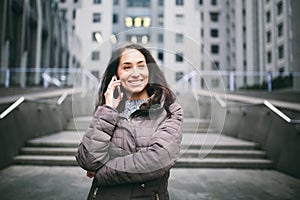 Young girl talking on mobile phone in courtyard business center. girl with long dark hair dressed in winter jacket in cold weather