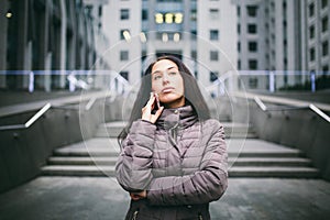 Young girl talking on mobile phone in courtyard business center. girl with long dark hair dressed in winter jacket in cold weather