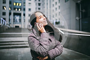 Young girl talking on mobile phone in courtyard business center. girl with long dark hair dressed in winter jacket in cold weather