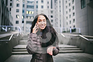 Young girl talking on mobile phone in courtyard business center. girl with long dark hair dressed in winter jacket in cold weather