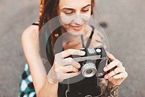 Young girl with tattoos and dreadlocks photographs vintage camera in the park