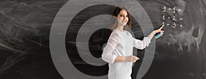 A young girl teacher or tutor is standing against the background of a chalk board with empty space for text. Math lesson