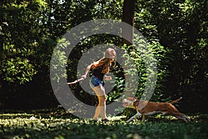 Young girl teasing her running dog with a branch