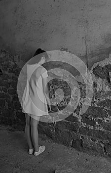 Young girl teenager with depression stands leaning against an old brick wall, vertical frame, copy space