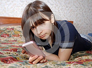 The young girl the teenager lies a bed with the cell phone. She communicates by the mobile phone by means of messengers and SMS