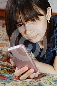 The young girl the teenager lies a bed with the cell phone. She communicates by the mobile phone by means of messengers and SMS