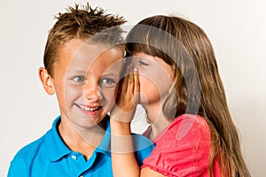 Young girl telling secret to young boy photo