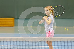Young girl on tennis court holding racquet, in photo