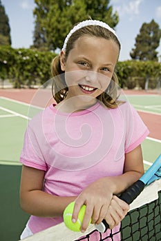 Young girl with tennis racket and ball by net at tennis court portrait