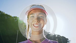 Young girl in the tennis uniform smiling to the camera.