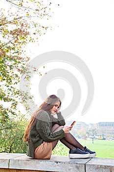 Young girl texting on phone sitting on stone fence