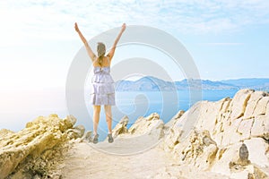 Young girl on top of a mountain near the sea. The traveler enjoys his vacation. Jump of a woman with happiness. Summer