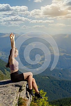 The young girl at the top of the mountain raised her hands up on blue sky background. The woman climbed to the top and enjoyed her