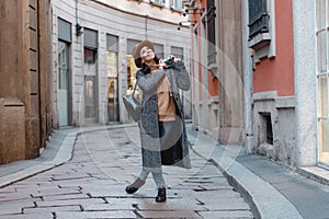 A young girl tourist in a fashionable brown hat is walking along a narrow street and taking pictures